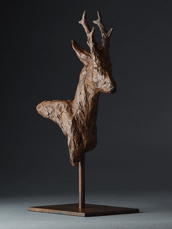 Sculpture of a deer's head and neck with antlers on a metal stand, set against a dark background.